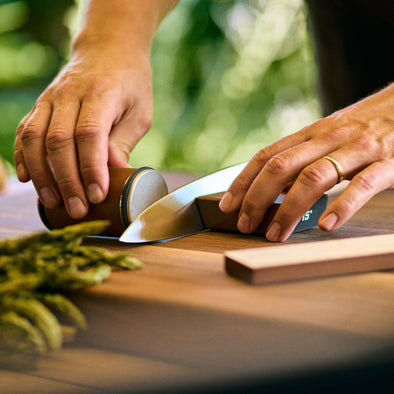 Hands operating a Test Tumbler Original Diamond rolling knife sharpener set on a wooden surface